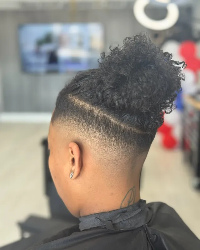 High skin fade with a hard part and curly top, cut at Top Style
