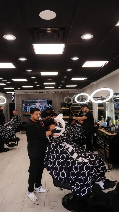 Barbers at work along the row of chairs, ring lights glowing