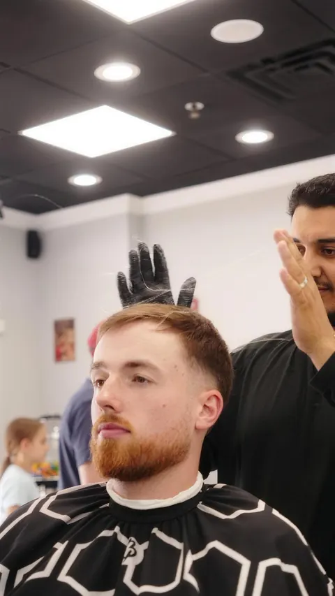 Client sitting up after a skin fade with a full beard, barber checking the shape