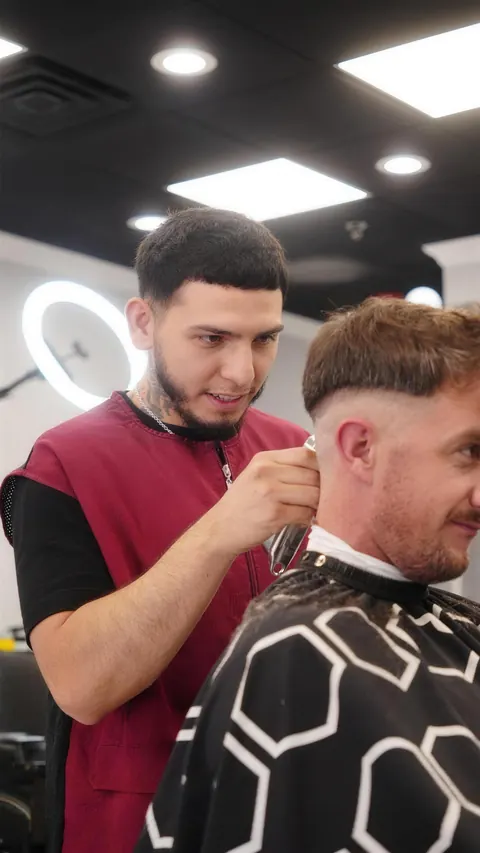 Barber in a red vest finishing a taper on a client with textured hair