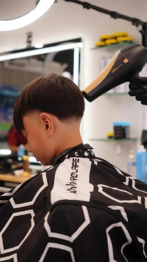 Barber blow-drying a boy’s crop before the final clean-up