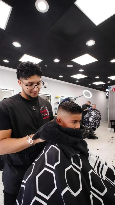 Barber cutting a young boy’s hair, a towel around his shoulders