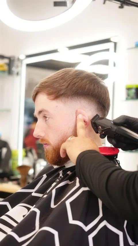 Barber blending a low fade at the temple into a full red beard